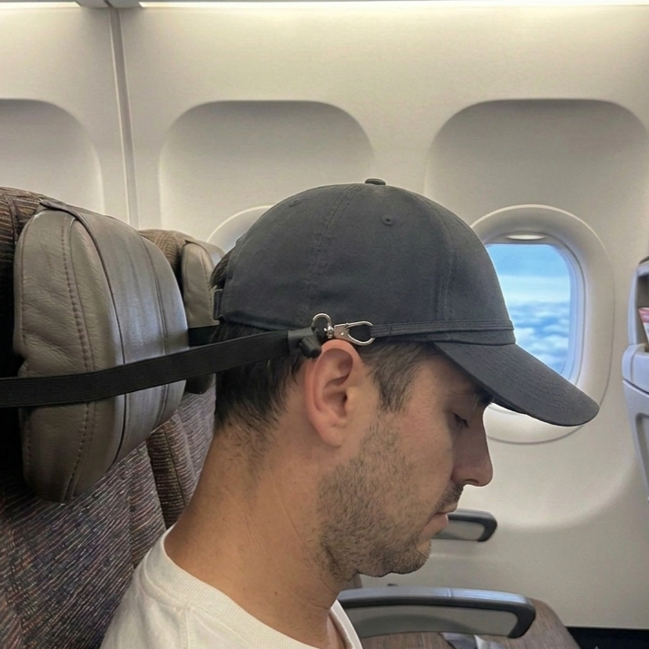 A man wearing  Dreaming Cap, seated in an airplane cabin next to a window and sleeping comfortably.